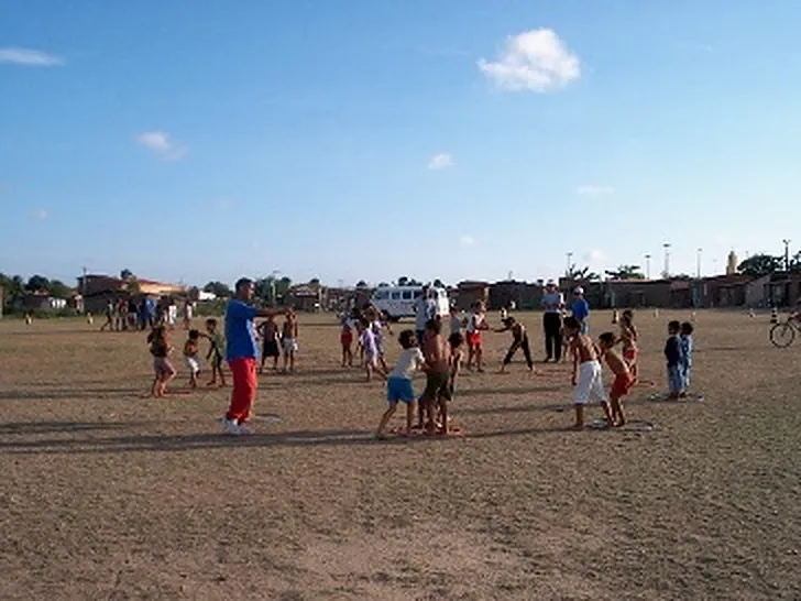 Kinderen doen een spel op een zandveld, een begeleider staat aan de kant en geeft aanwijzingen.
